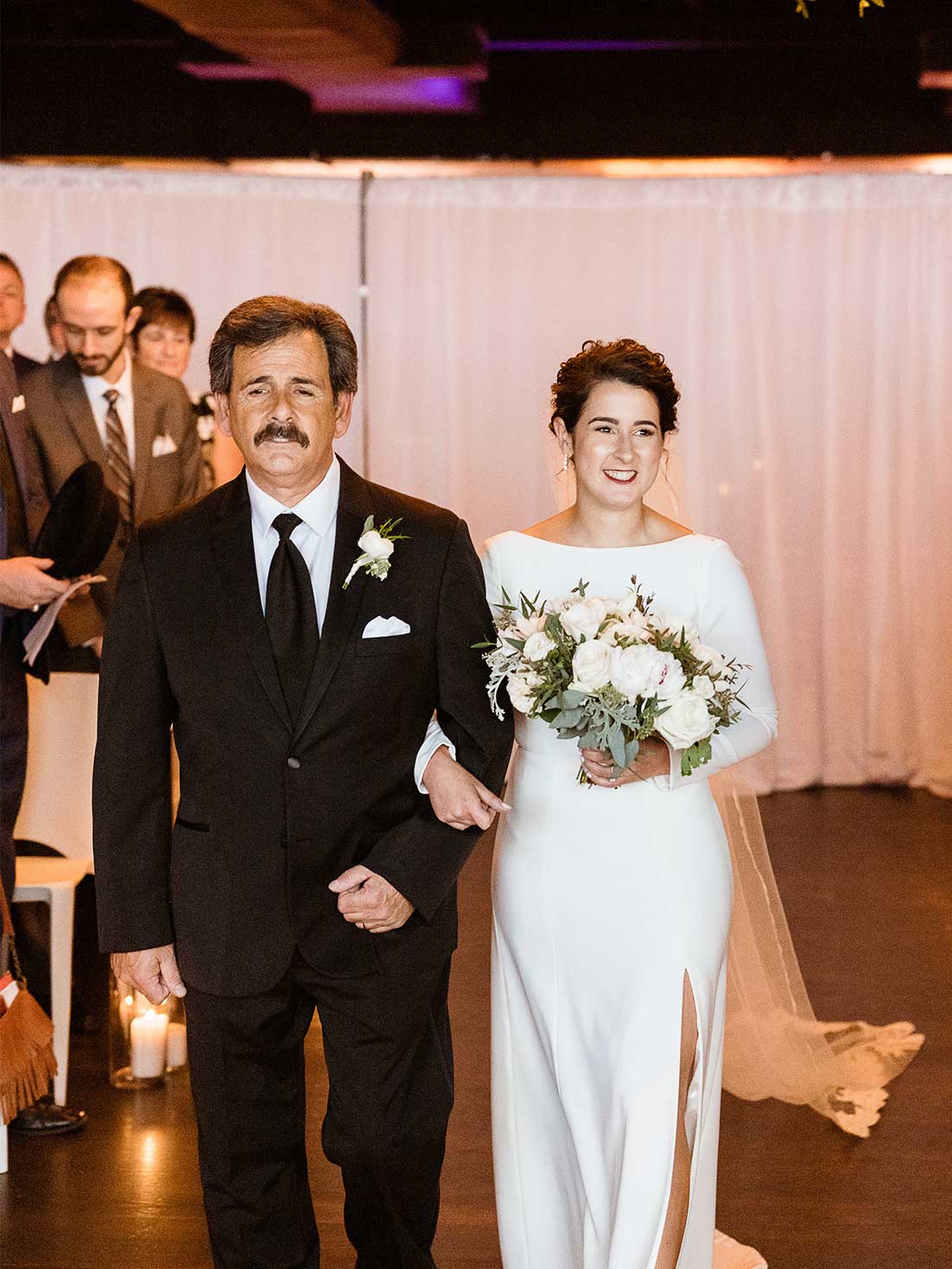 Smiling bride is escorted down the ceremony aisle by her father